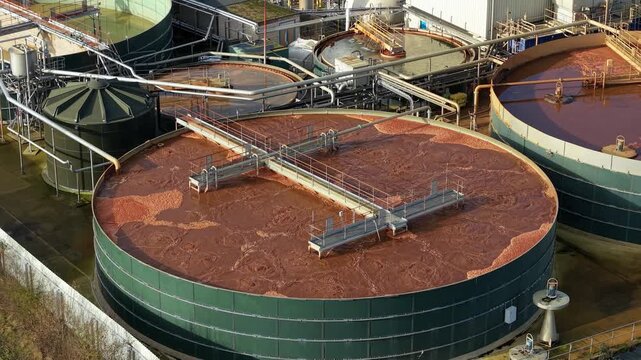 Aerial view of industrial water treatment tanks with brown liquid contrasting against the green containers, Sutton Bridge, Spalding, United Kingdom.