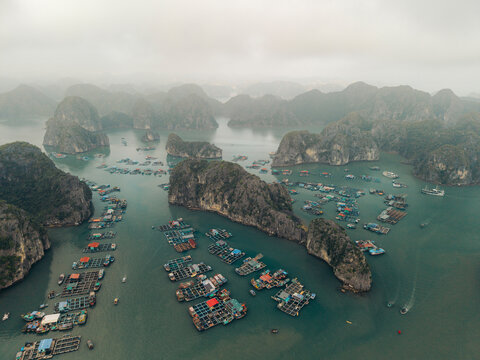 Aerial view of floating fishing village amidst limestone karsts in a calm, misty bay. Lan Ha Bay, Cat Ba, Vietnam