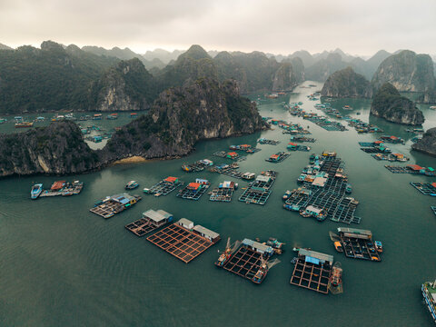 Aerial view of floating fishing villages surrounded by limestone islands in calm green waters. Lan Ha Bay, Cat Ba, Vietnam