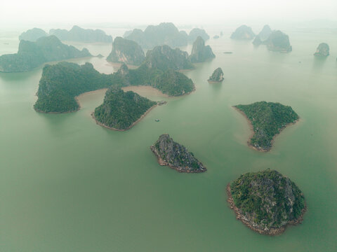 Aerial view of lush green islands rising from a serene emerald sea under a hazy sky. Lan Ha Bay, Cat Ba, Vietnam