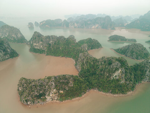 Aerial view of lush green islands with rocky cliffs in a misty, calm blue-green sea. Lan Ha Bay, Cat Ba, Vietnam
