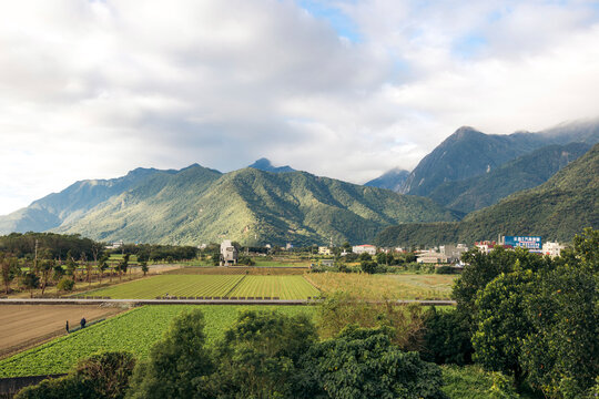 Expansive view of lush green fields and distant mountains under a partly cloudy sky. Xincheng Township, Hualien County, Taiwan
