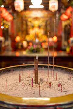 Lit incense sticks in a pot with a blurred golden temple in the background. Hualien County, Taiwan