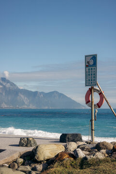 Coastal view with safety sign and life buoy near rocky shore under clear blue sky. Hualien County, Taiwan