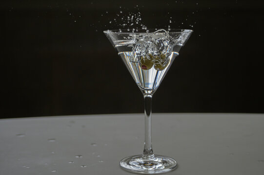 Martini cocktail splash with olive garnish falling into it action freeze, isolated on a black and white background, Portrait shot, two olives cocktail