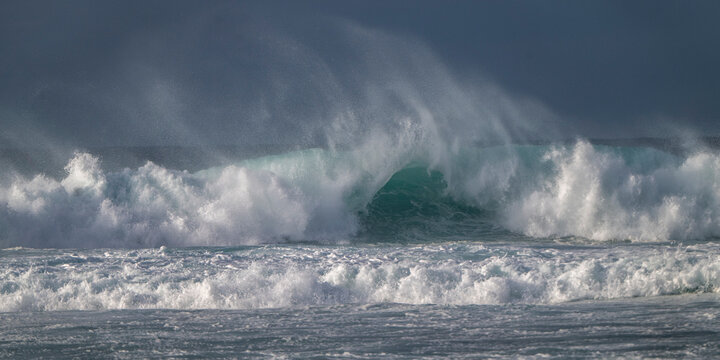 Powerful ocean waves crash with misty spray under a dramatic sky. Paia, Hawaii, USA