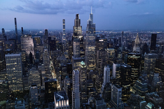Aerial view of city skyline at dusk with illuminated skyscrapers under a cloudy sky. Manhattan, New York, USA