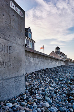 Coastal houses and an American flag along a rocky shoreline under a blue sky. Marshfield, MA, USA