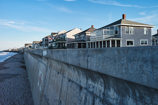 Seaside houses with wooden exteriors lined along a concrete seawall on a bright day. Marshfield, MA, USA