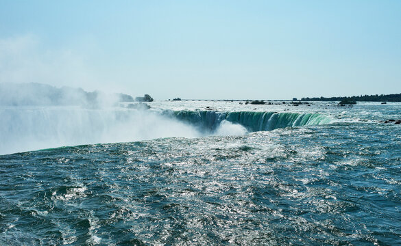 Massive waterfall with mist under sunny blue sky and rocky edges in the background. Niagara Falls, Ontario, Canada