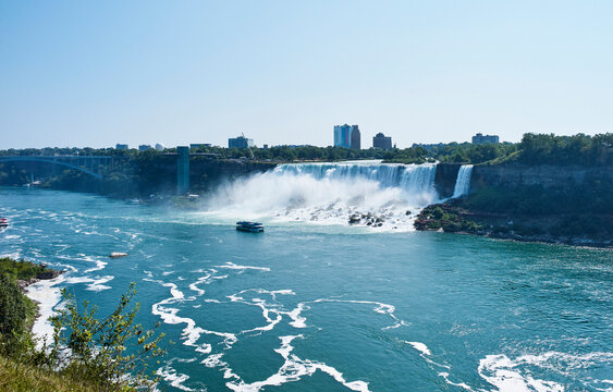Majestic waterfall cascading over cliffs with boats in the river framed by a city skyline. Niagara Falls, Ontario, Canada