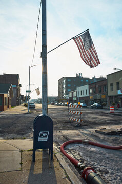 Urban street with construction, American flag, and postal mailbox under blue sky. Escabana, Michigan, USA