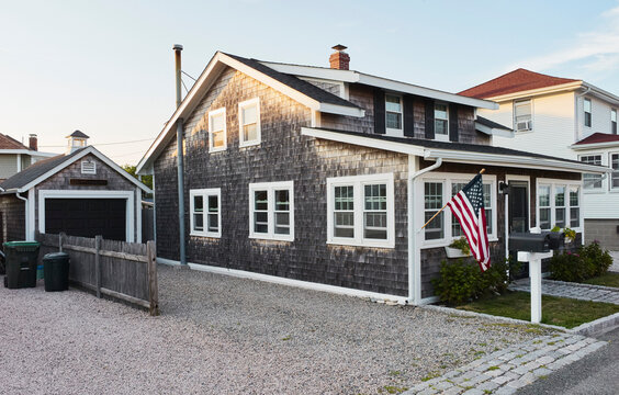 Charming rustic house with wood siding and American flag on quiet suburban street at sunset. Marchfield; Massachusetts, USA