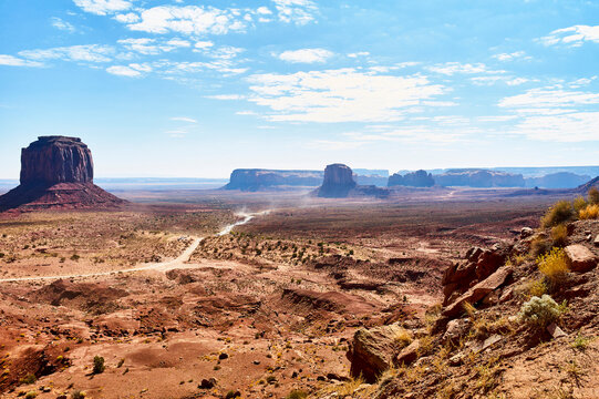 Vast desert landscape with iconic buttes under a bright, partly cloudy blue sky. Monument Valley, Arizona, USA