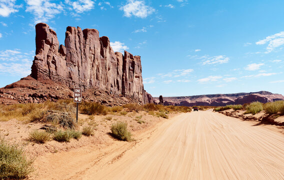 Desert road leads to stunning red rock formations under a clear blue sky. Monument Valley, Arizona, USA