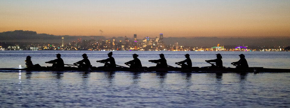 Rowing team silhouetted against city skyline at dusk, peaceful water reflects lights. WA, USA