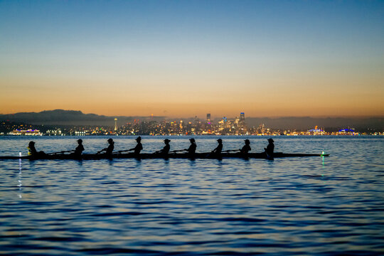 Rowing team silhouetted against a vibrant cityscape at dawn on calm water.   WA, USA
