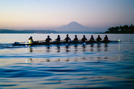 Rowing team glides across tranquil lake at sunrise with mountain in the background. WA, USA