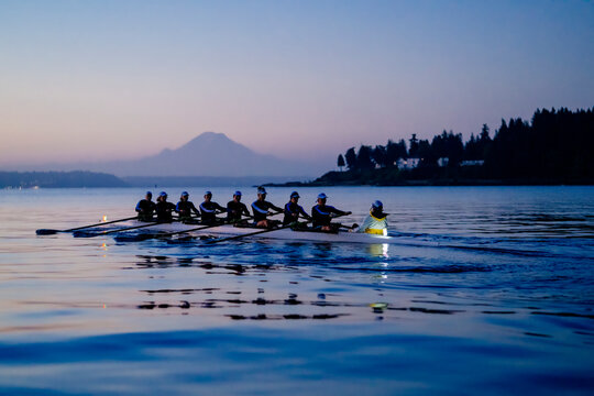 Seven rowers glide on a calm lake at dawn with a distant mountain visible under a serene sky. WA, USA
