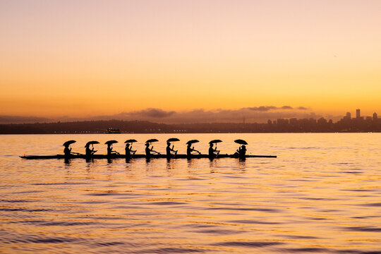 Rowing team glides on serene water at sunset, city skyline silhouetted in the background. WA, USA