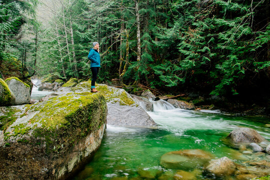 Person standing on moss-covered rock by a vibrant green river in a lush forest. Deception Falls, Pacific Northwest, WA, USA