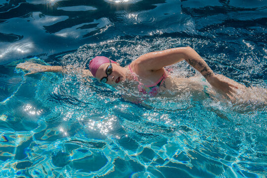 Woman swimming freestyle in a pool with a pink swim cap and goggles. USA