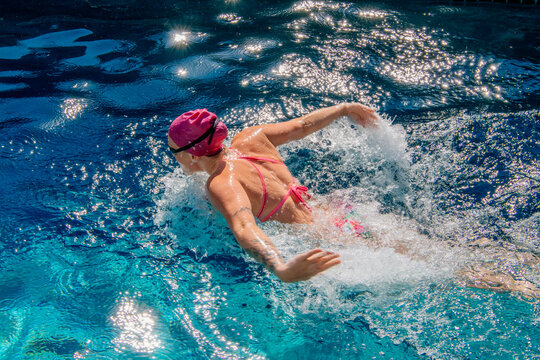 Swimmer in a pink swimsuit and cap doing the butterfly stroke in a sunlit swimming pool. USA