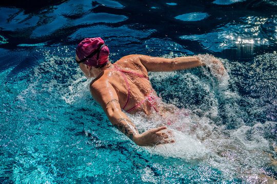 Swimmer in pink cap doing butterfly stroke in vibrant blue water pool capturing splash and action. USA