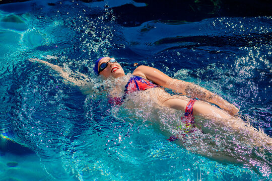 Swimmer doing backstroke in a vibrant blue pool under sunlight. USA