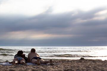 Romantic Couple Lying on Sandy Beach Watching Ocean Waves at Sunset
