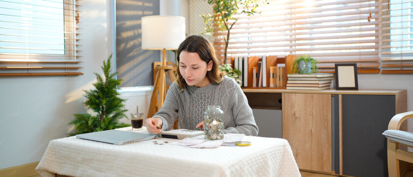 Saving money wealth concept, young woman hand putting coin into jar for saving cost, cash finance planning to spend enough money on her income for save money, payment tax, investing
