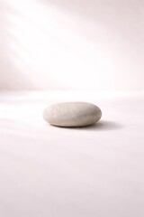 One gray stone on white table background with sun light and shadow for cosmetic product display