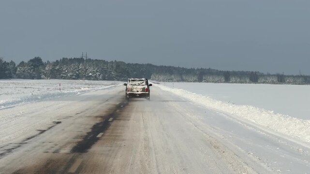 A car is driving along a road in winter. The road is covered with snow.