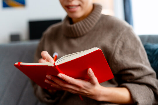 Woman holding a red notebook, writing notes and planning tasks with a pen