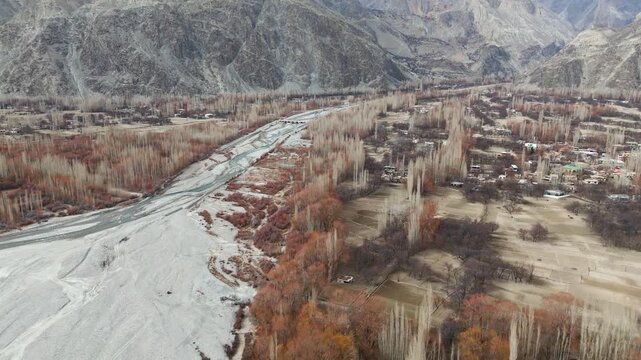 Aerial view of a river cutting through a valley, flanked by bare trees and mountains, creating a stark, natural landscape, Daghoni Balgar, Gilgit Baltistan, Pakistan.