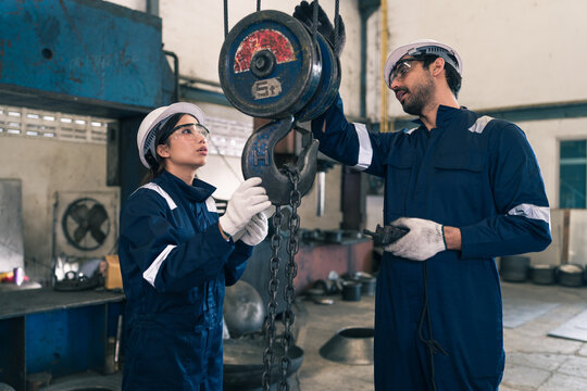 Diverse Man and woman engineer wearing safety uniform hardhat inspecting heavy lifting crane hook factory production line professional technician team working warehouse manufacturing plant maintenance
