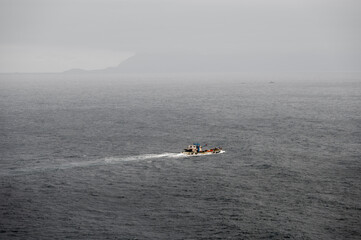 A small boat floats on the East China Sea on a cloudy, hazy day, with distant land barely visible on the horizon, creating a quiet, minimalist seascape with a calm and moody atmosphere.

