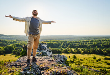 Young man with outstretched arms standing on top of a rock in Jura Poland enjoying summer day