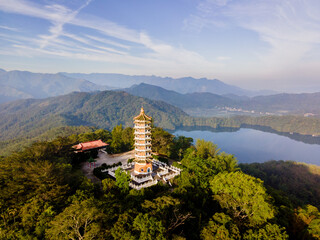 Aerial view of Ci En Pagoda rising above forested hills at Sun Moon Lake, Taiwan, with the blue lake and surrounding mountains in the background on a clear, sunny day.

