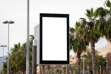 Blank vertical digital billboard with white screen mockup advertising template, standing outdoors in an urban street against palm trees backdrop, ready for content display