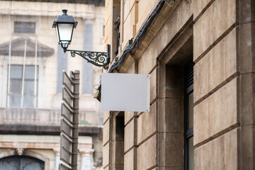 Blank white signage mock-up on a classic stone building facade, showcasing a traditional wrought iron street lamp, offering clear space for branding and messaging in an urban setting
