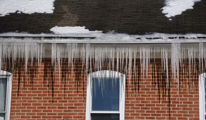 Long icicles formed on the edge of a snow-covered roof, showing winter freeze and potential ice-dam formation.