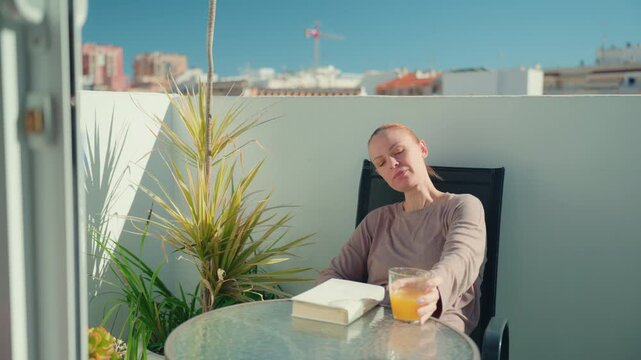 Quiet moment of mental rest at home. Woman reading book, drink glass of fresh orange juice and relax indoors. Mental health, self care, emotional balance and calm lifestyle concept.