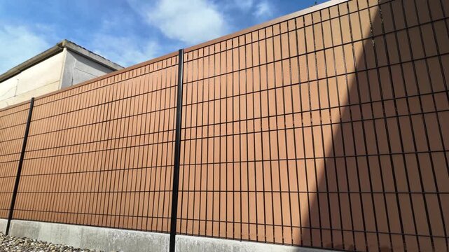 Smooth tilt shot of a modern black rigid mesh fence with WPC composite wood privacy slat and concrete base outdoors. Side view.
