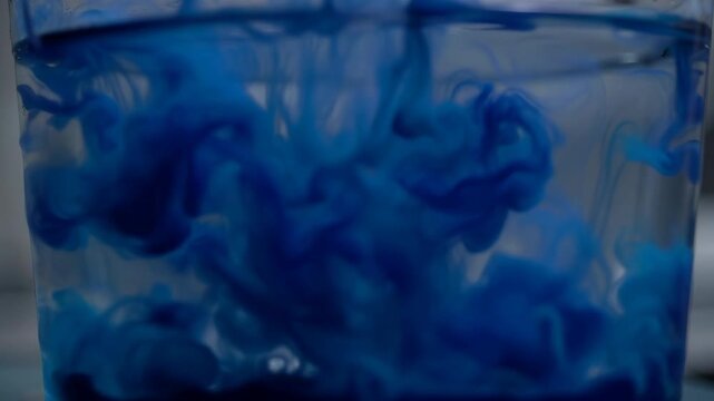 Abstract blue ink dissolving slowly in clear water creating swirling patterns and visual effects for backgrounds
