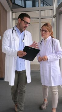 Male and female doctors discussing patient report while walking