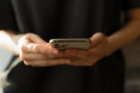 Сlose-up of hands interacting with a smartphone. The person is holding the device in his hands. The background is blurry, creating a neutral atmosphere and focusing on the action.