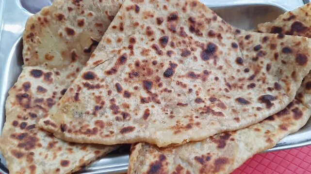 Pan shot of aloo paratha or flatbread served with creamy curd, onions, and crisp cucumber slices