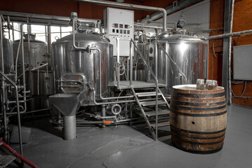 Stainless steel brewing tanks and a wooden barrel dominate this industrial brewery scene.