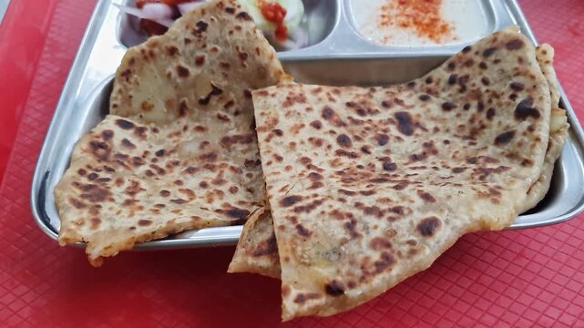 Pan shot of aloo paratha or flatbread served with creamy curd, onions, and crisp cucumber slices